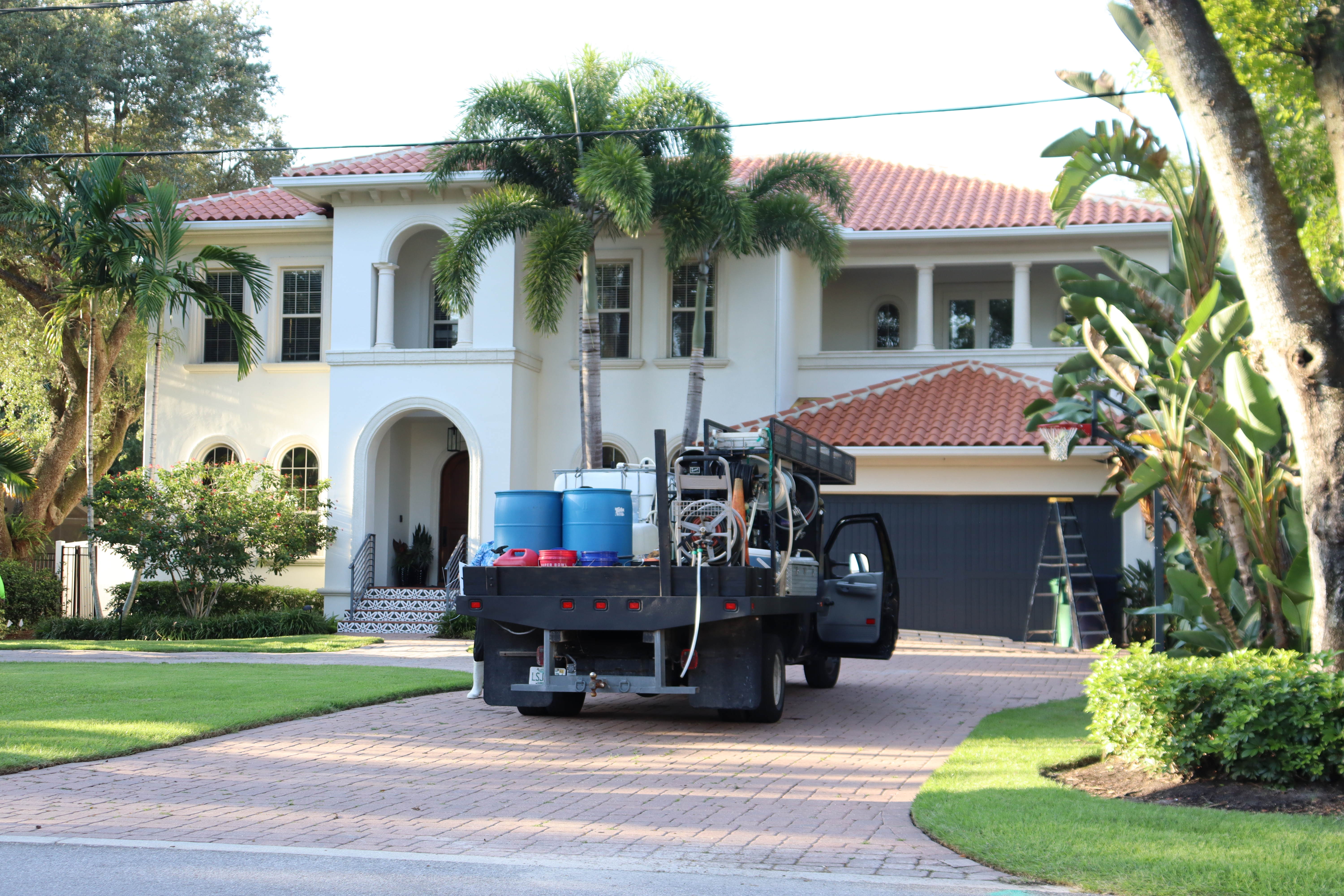 A hyper-realistic, bright, sunlit shot of a professional pressure washing setup in an affluent neighborhood. High-contrast, clean, professional home service aesthetic, vibrant blue skies, welcoming.