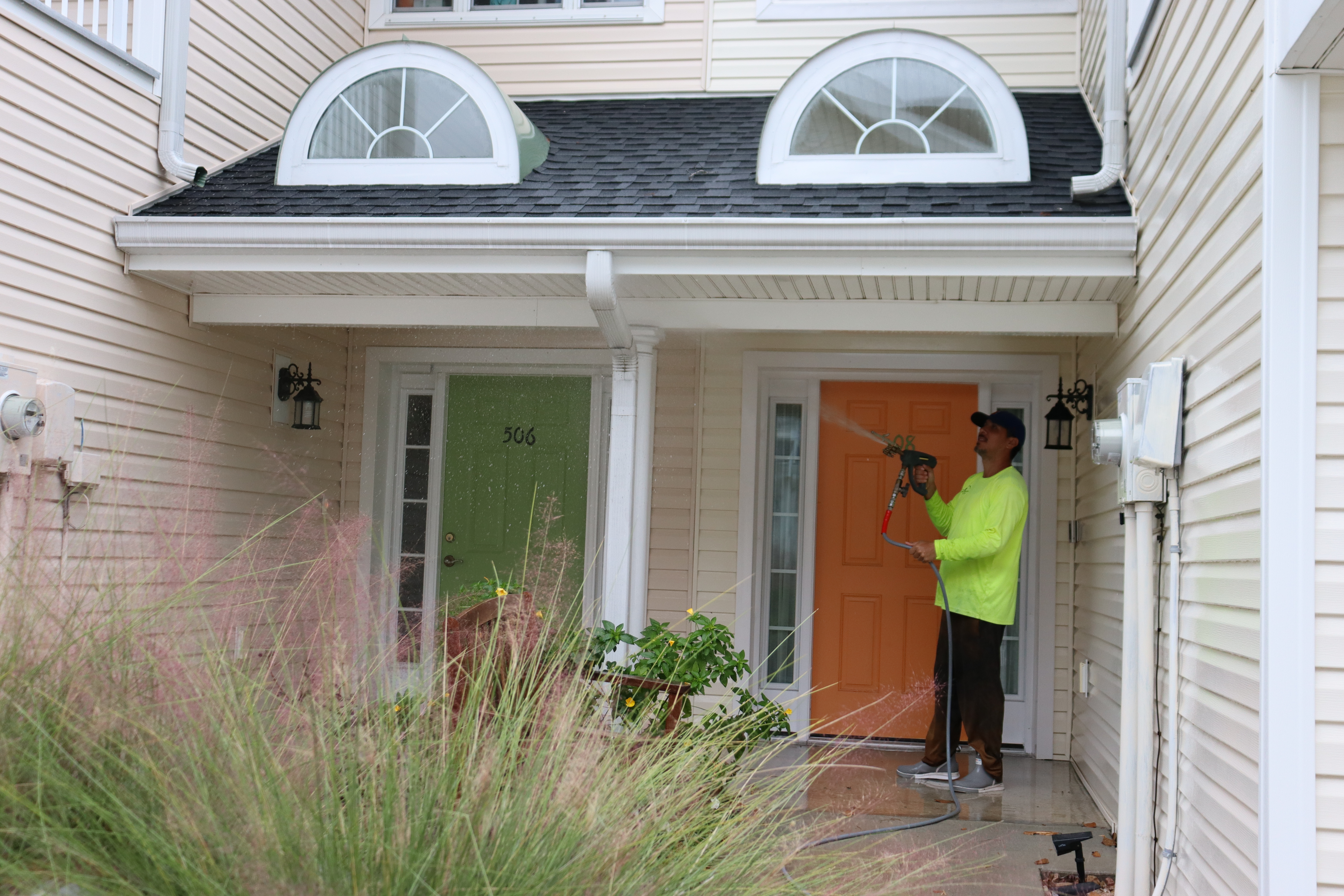 A hyper-realistic, bright, sunlit shot of a professional soft washing technician safely cleaning a house exterior. High-contrast, clean, professional home service aesthetic, vibrant blue skies, welcoming.