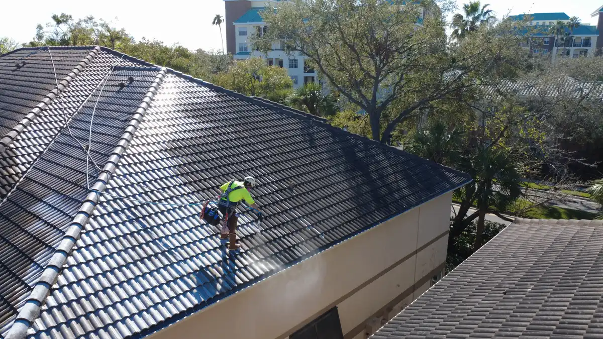 Aerial drone photo of Brian Vasquez in OSHA 100% tie-off safety harness and helmet soft washing a multi-building HOA barrel tile roof complex in Pinellas County, Florida